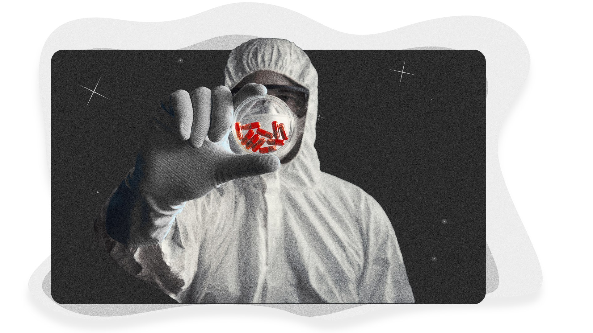 Person in a PPE suit holding a petri dish with red pills inside